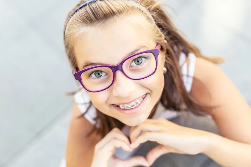 A smiling girl in purple glasses showing her braces