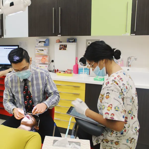 A Kids Dental specialist treating a young patient while a dental assistant records notes